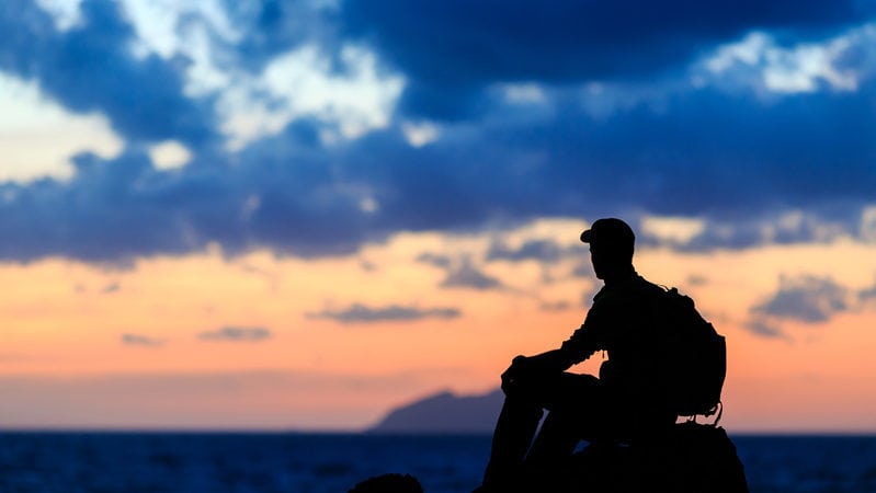 Man sitting on mountain with blue sky in the background.